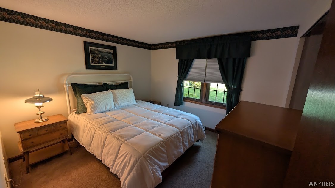 Bedroom with a white-quilted bed, dark green curtains, and a window overlooking the lawn.