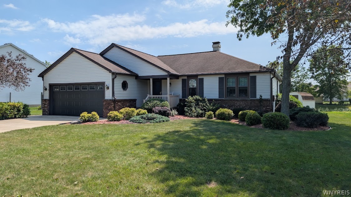 Single-story home with an attached garage, brick facade, landscaped shrubs, and a shaded front lawn.