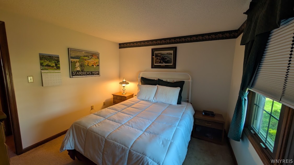 Bedroom with a white quilted bed, golf artwork, and a window overlooking a green lawn.