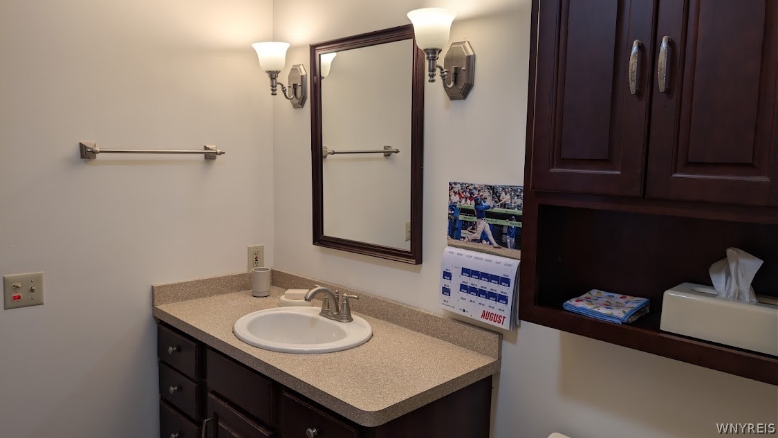 Bathroom vanity with an oval sink, beige countertop, and dark wood cabinetry.