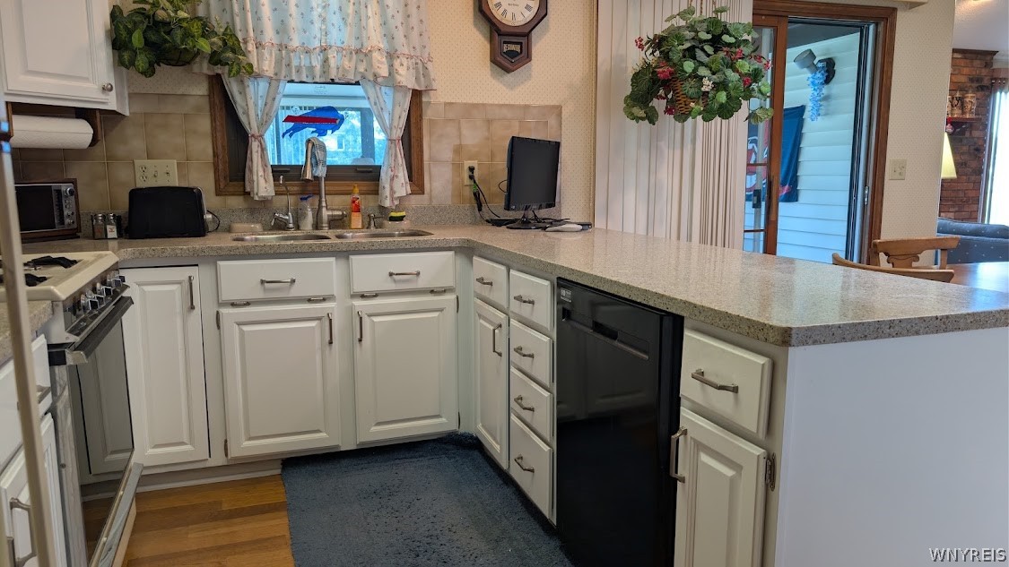 Kitchen with white cabinets, gray countertops, a peninsula, and a black dishwasher.