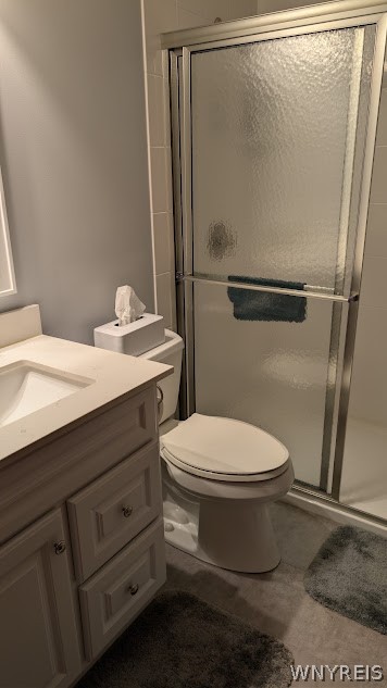 Bathroom with gray vanity, toilet, frosted-glass shower, and gray bath mat.