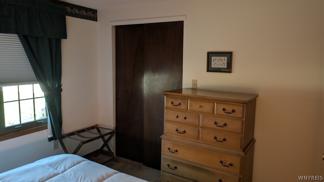 Bedroom with a wooden dresser, dark wood door, and curtained window.