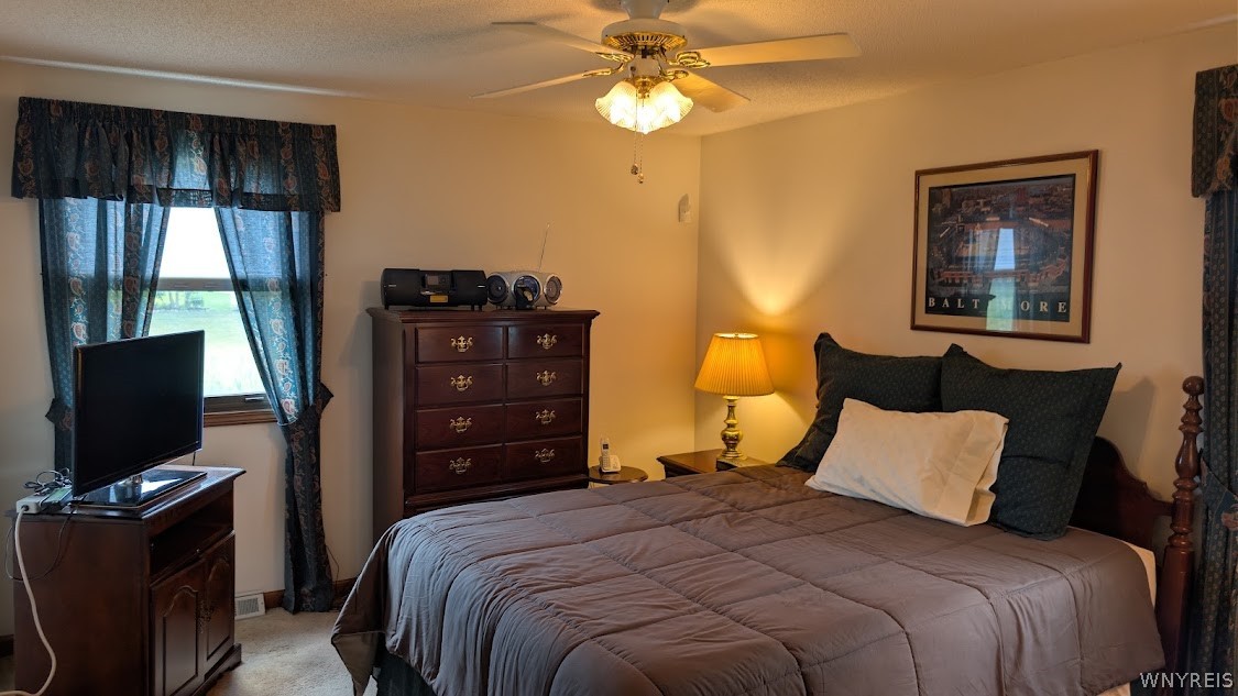 Furnished bedroom with a large bed, dark wood dresser, and television beside a curtained window.