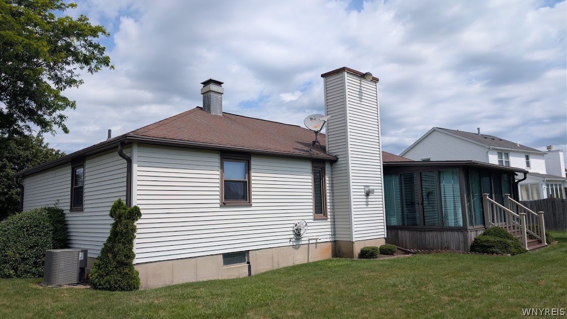 Rear of a gray-sided house with a tall chimney, enclosed sunroom, and broad lawn.