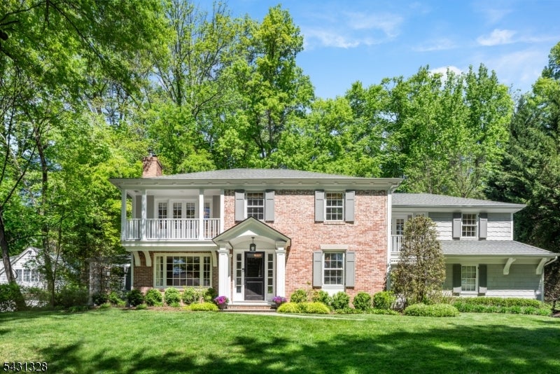 Two-story brick house with a covered balcony, white shutters, and a broad green lawn.