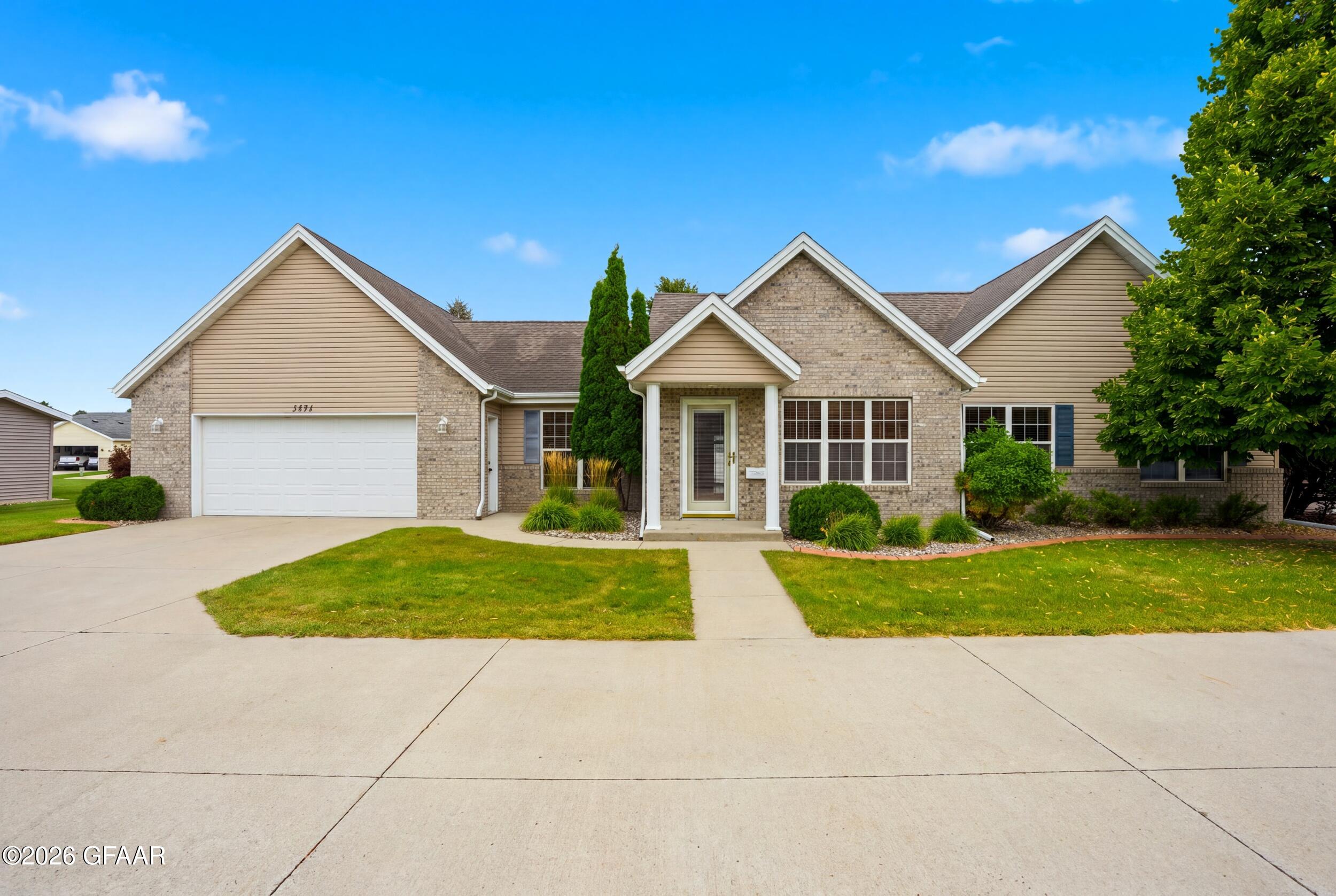 Single-story brick and tan-sided home with a two-car garage, covered entry, and landscaped lawn.