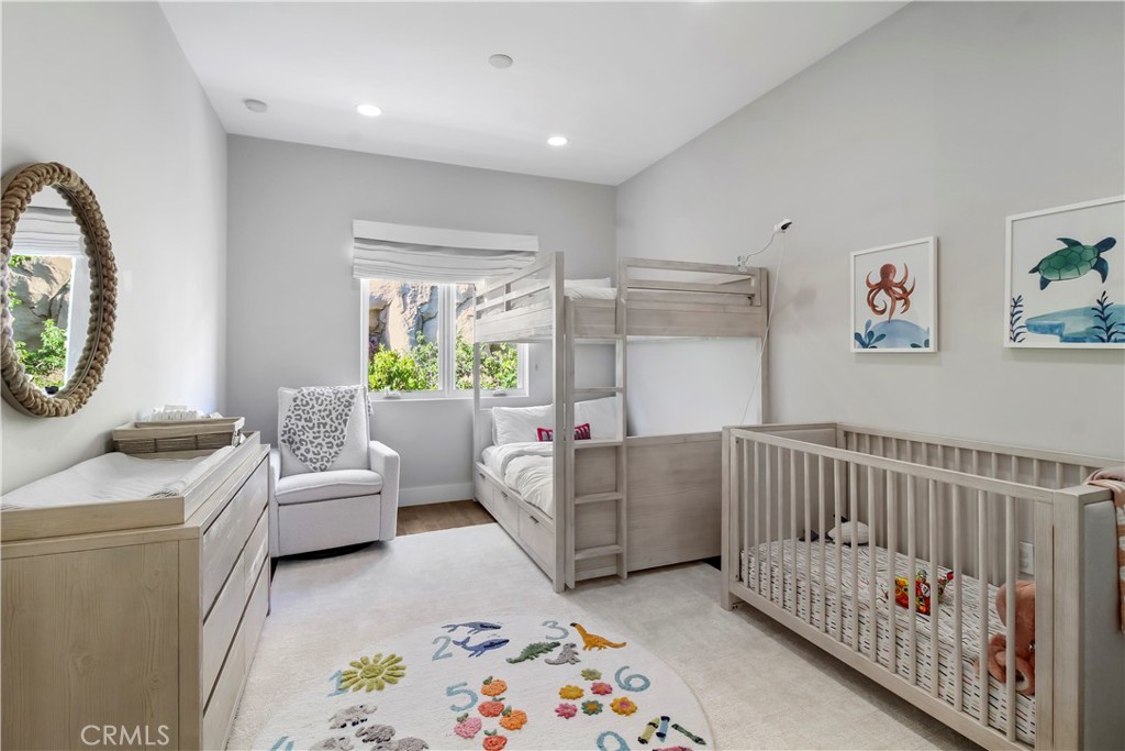 Nursery with a wooden bunk bed, crib, changing table, and colorful animal rug.
