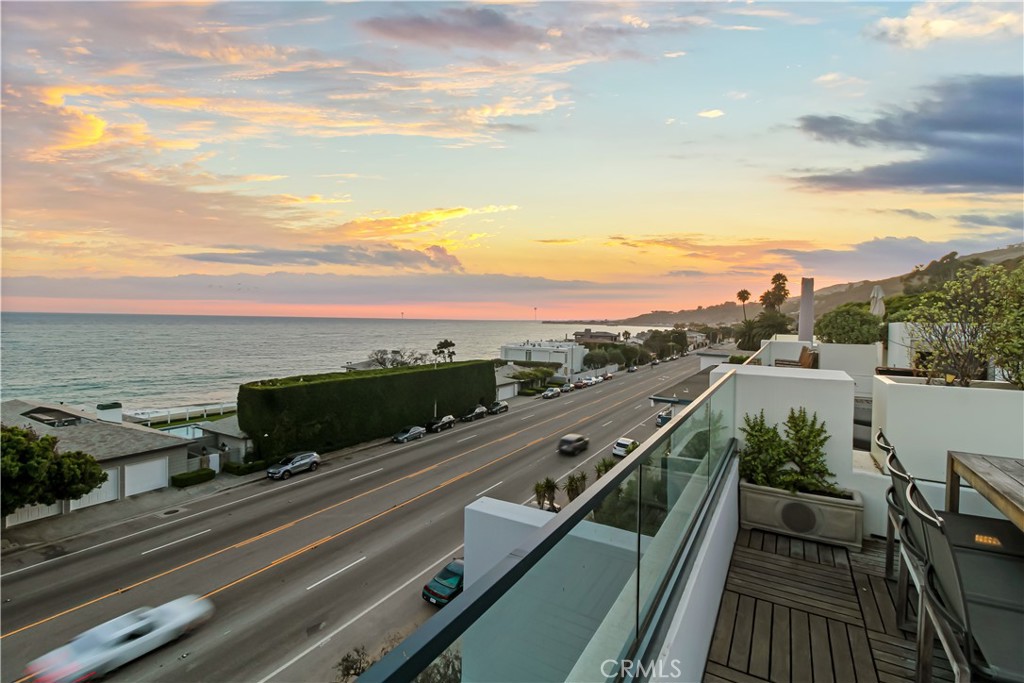 Oceanfront terrace overlooking Pacific Coast Highway at sunset, with glass railing and wood decking.