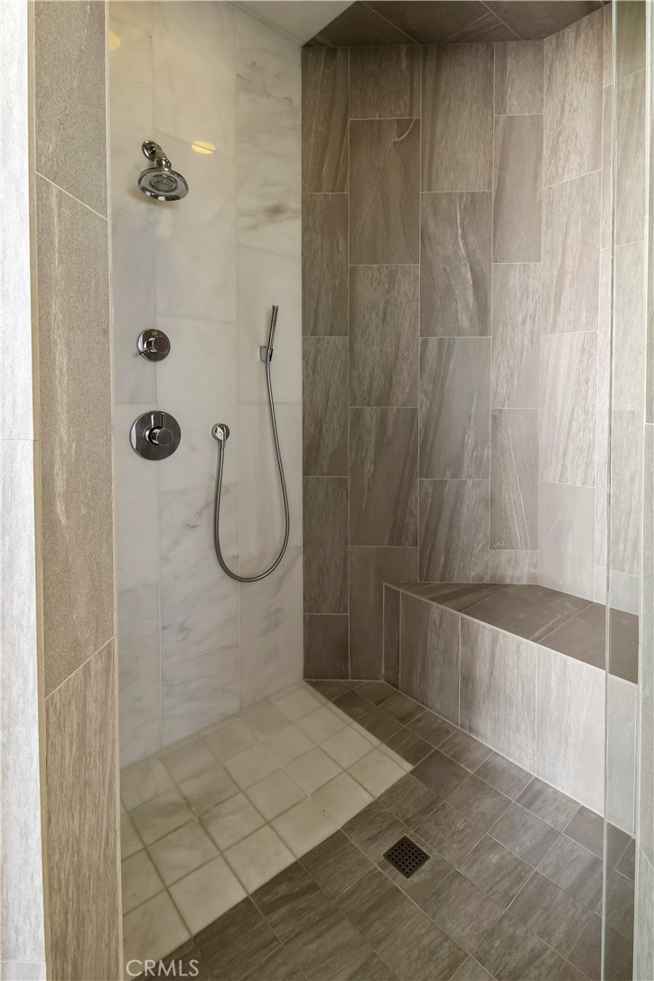 Walk-in shower with gray tile, a built-in bench, and handheld shower wand.