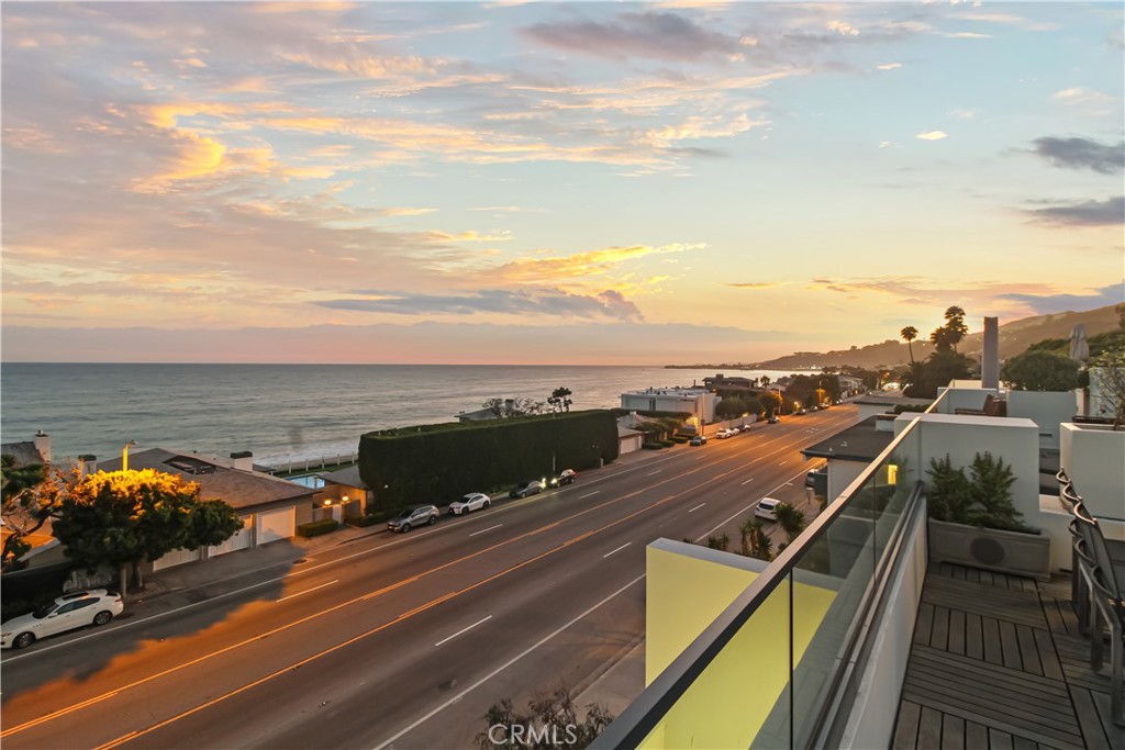Coastal view from a balcony overlooking the Pacific Ocean and Pacific Coast Highway at sunset.