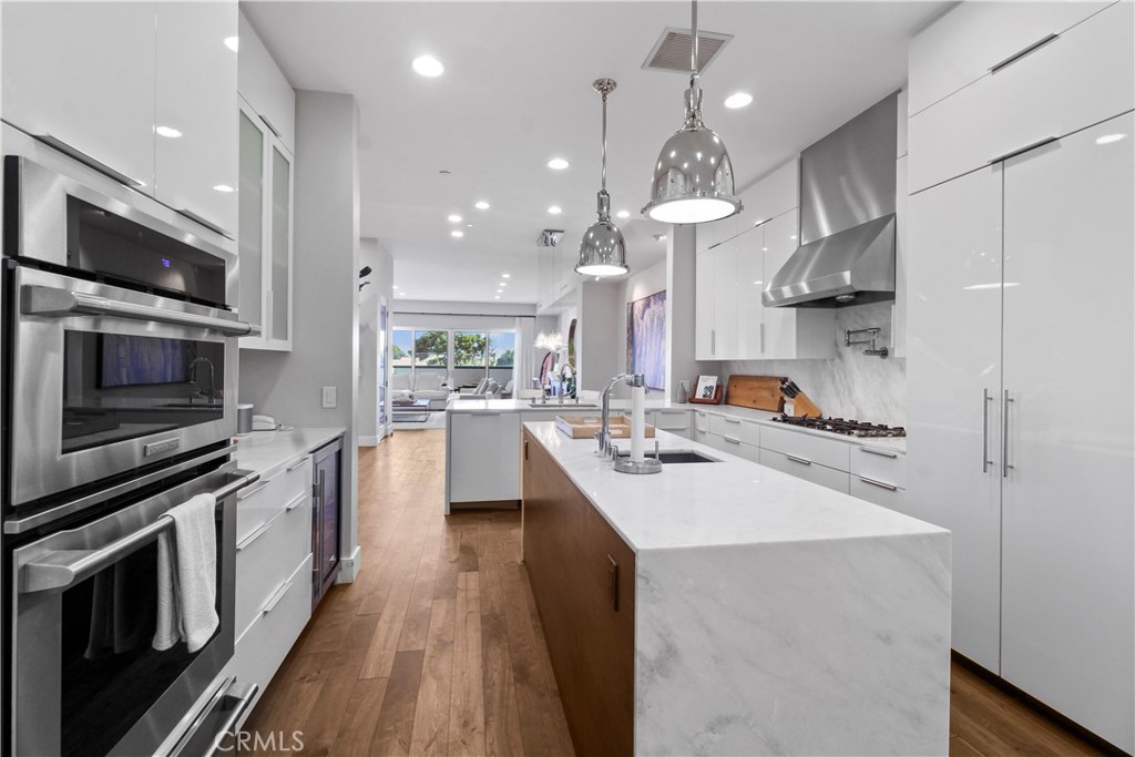 Modern white kitchen with a marble waterfall island, stainless steel double ovens, and pendant lights.