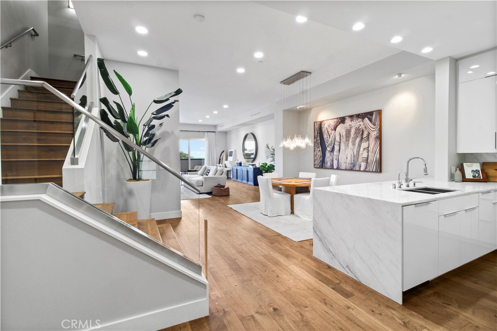 Open-plan kitchen with a marble island, glass-railed staircase, and adjoining dining and living areas.