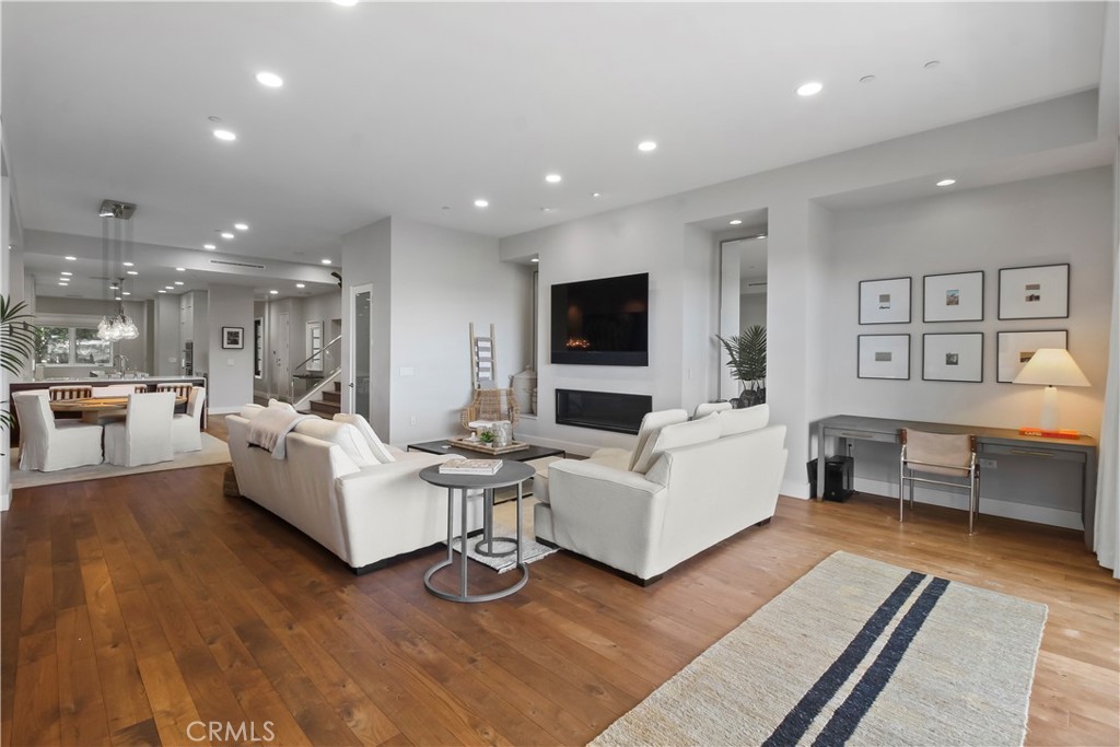 Open-plan living room with white sofas, a fireplace, wood floors, and adjoining dining area.