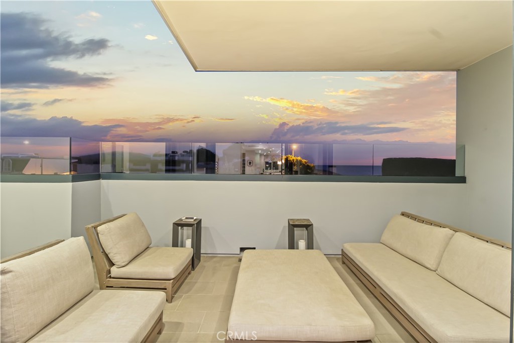 Ocean-view terrace with cream lounge seating and glass railing at sunset.