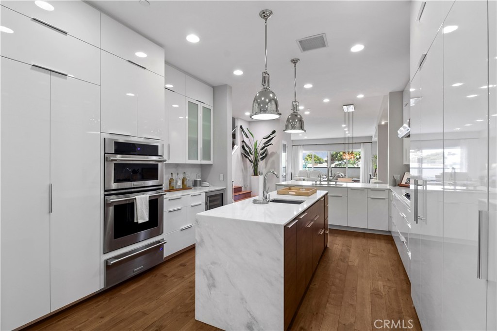 Modern kitchen with glossy white cabinets, stainless steel ovens, and a marble island.
