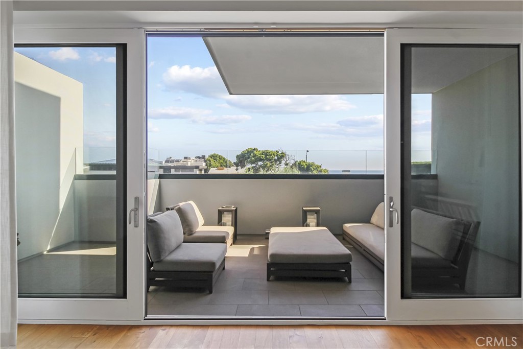 Modern terrace with lounge seating and a distant ocean view through sliding glass doors.