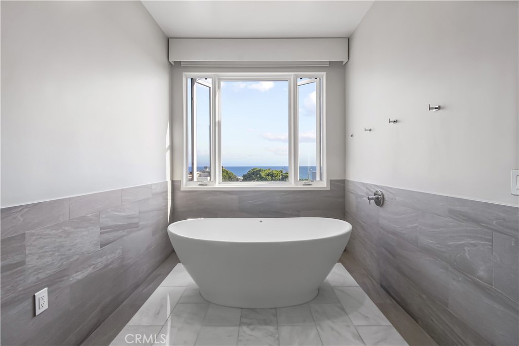 Bathroom with a freestanding tub beneath a window overlooking the ocean.
