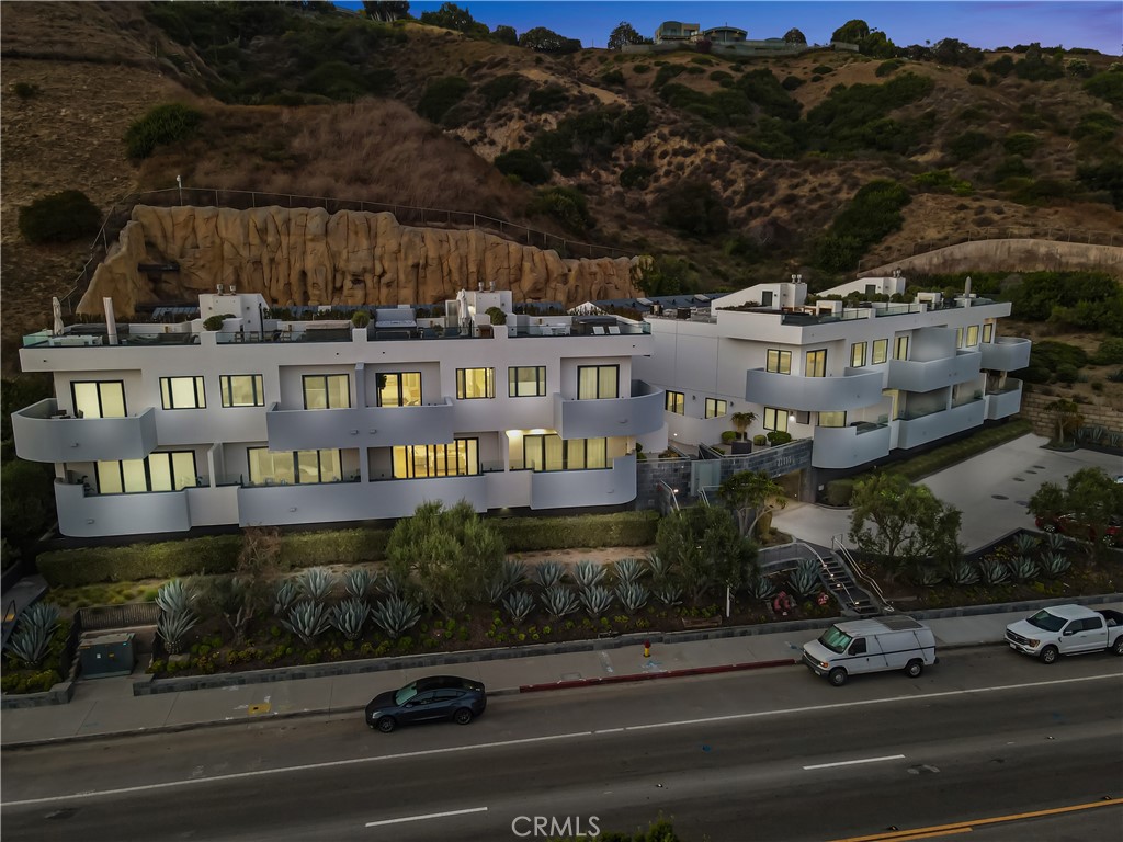 Modern white multi-unit building with balconies against a hillside, viewed from above Pacific Coast Highway.