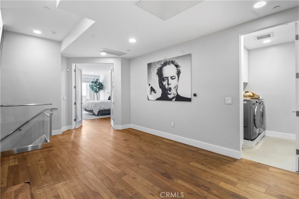 Interior landing with hardwood floors, bedroom doorway, laundry room, and a large black-and-white wall portrait.