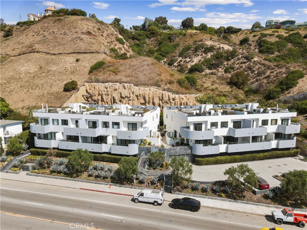 Modern white residential building along Pacific Coast Highway, backed by dry hills.