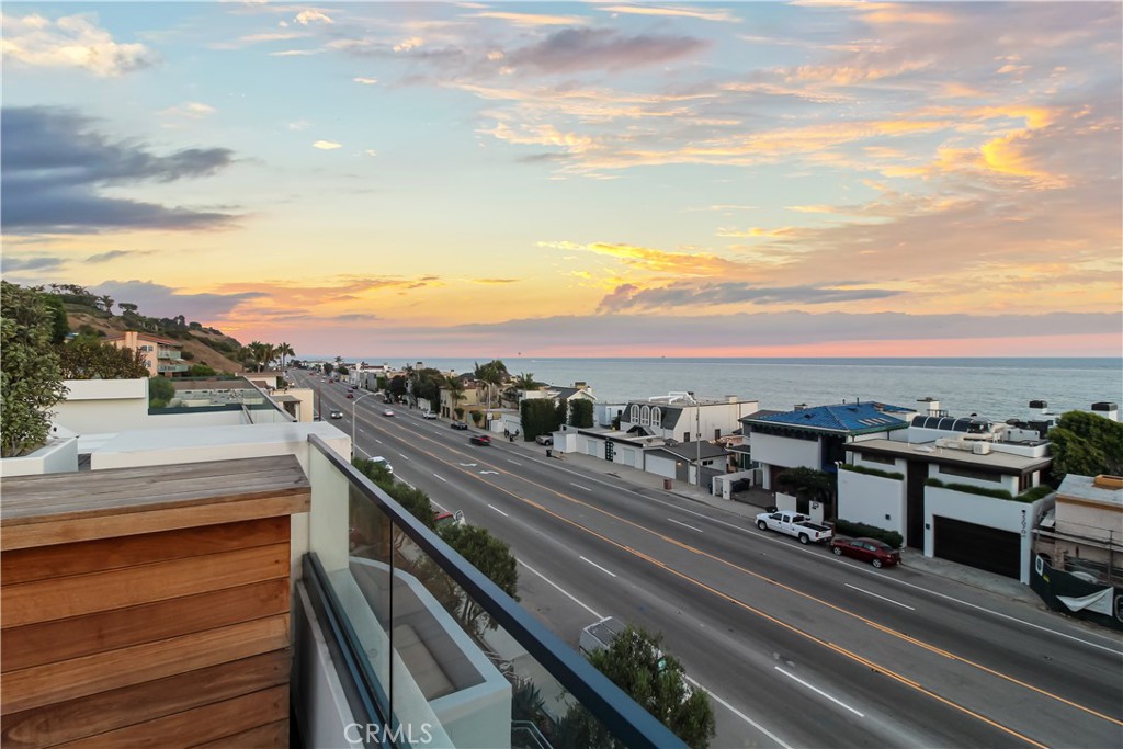 Ocean view from a balcony over Pacific Coast Highway, with coastal homes beneath a colorful dusk sky.