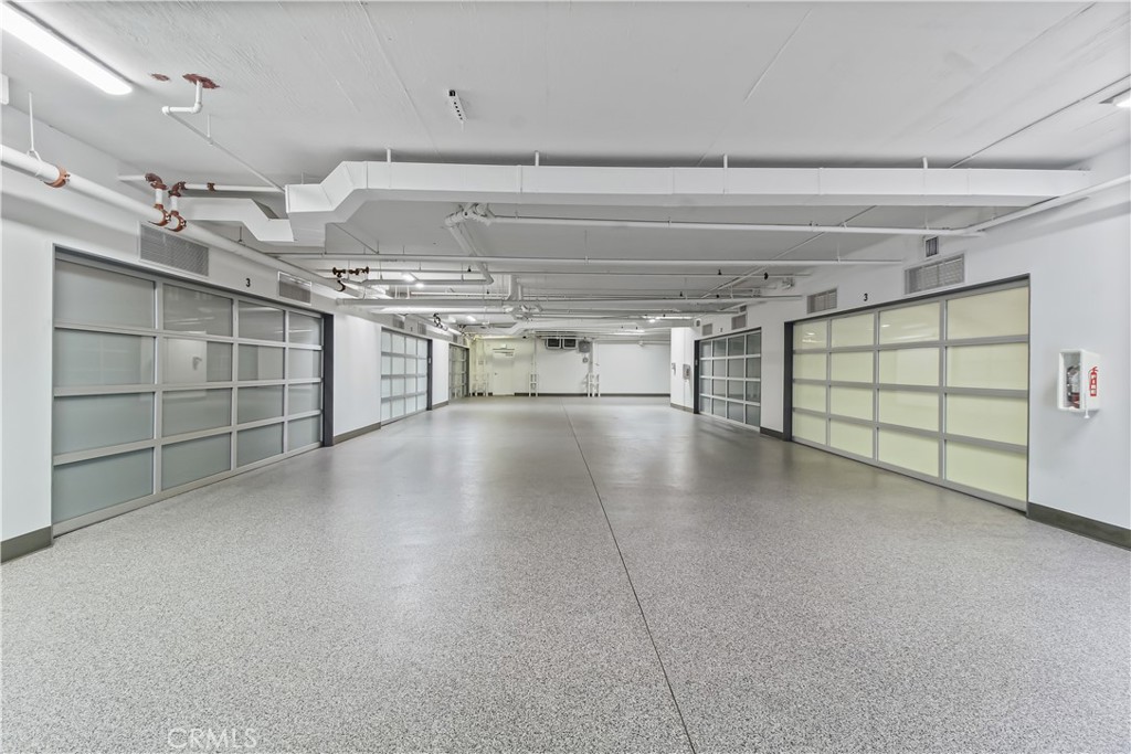 Empty garage with translucent-paneled doors, a speckled floor, and exposed ceiling ducts.