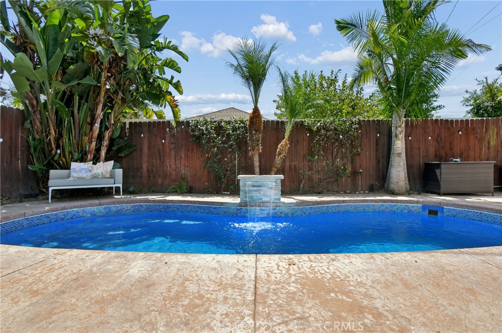 Backyard pool with a raised tiled water feature, stone deck, and tropical palms.