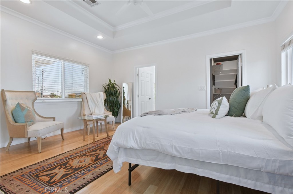 Staged bedroom with a large white bed, tray ceiling, hardwood floors, and patterned runner rug.
