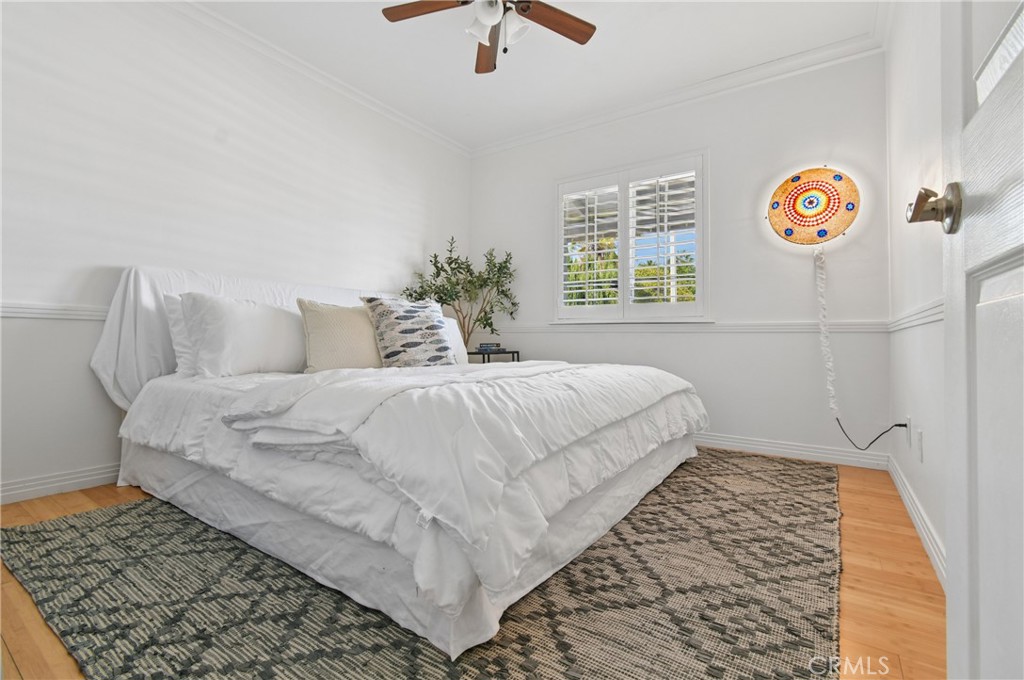 Bedroom with a white bed, plantation shutters, patterned rugs, and a colorful circular wall lamp.