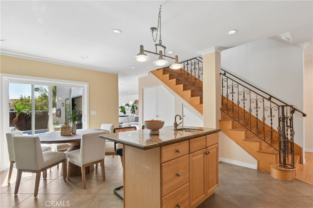 Kitchen and dining area with a granite island beside a wood staircase with ornate iron railings.