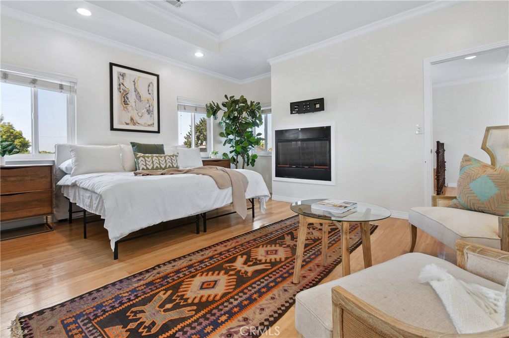 Staged bedroom with a white bed, wall fireplace, patterned rug, and sitting area.