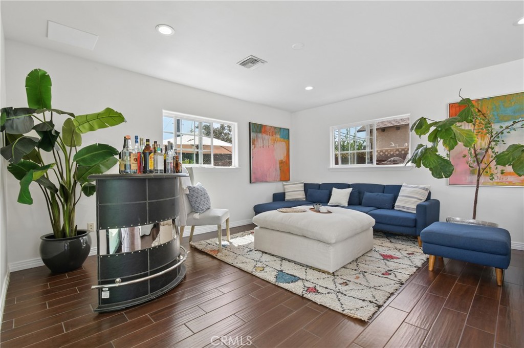 Living room with a blue sectional, white ottoman, patterned rug, and curved bar cabinet.