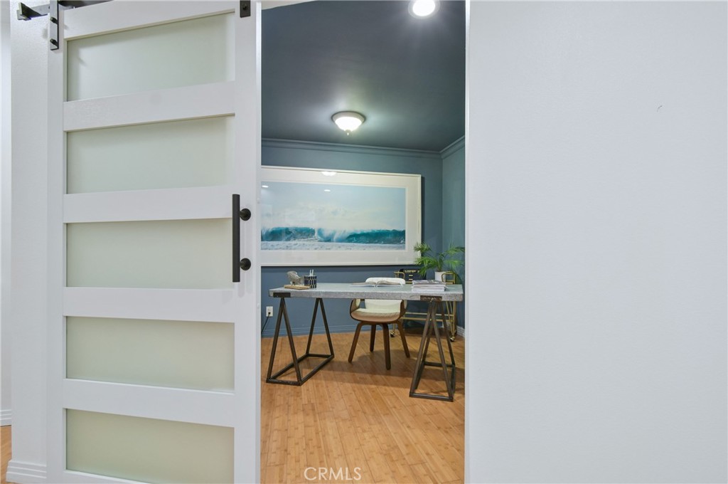 Staged home office with blue-gray walls, hardwood floors, and a desk viewed through an open sliding door.