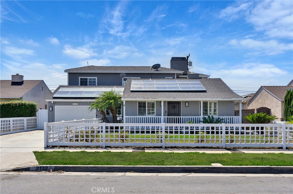 Gray home with rooftop solar panels, a white picket fence, and a small front yard.