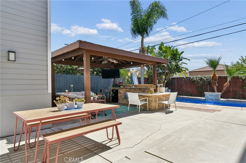 Backyard patio with a pergola-covered outdoor kitchen, picnic table, and swimming pool.