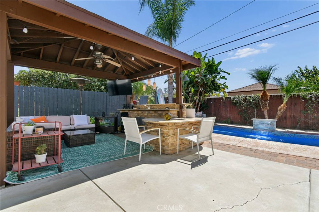 Covered backyard patio with stone outdoor kitchen, lounge seating, and a swimming pool.