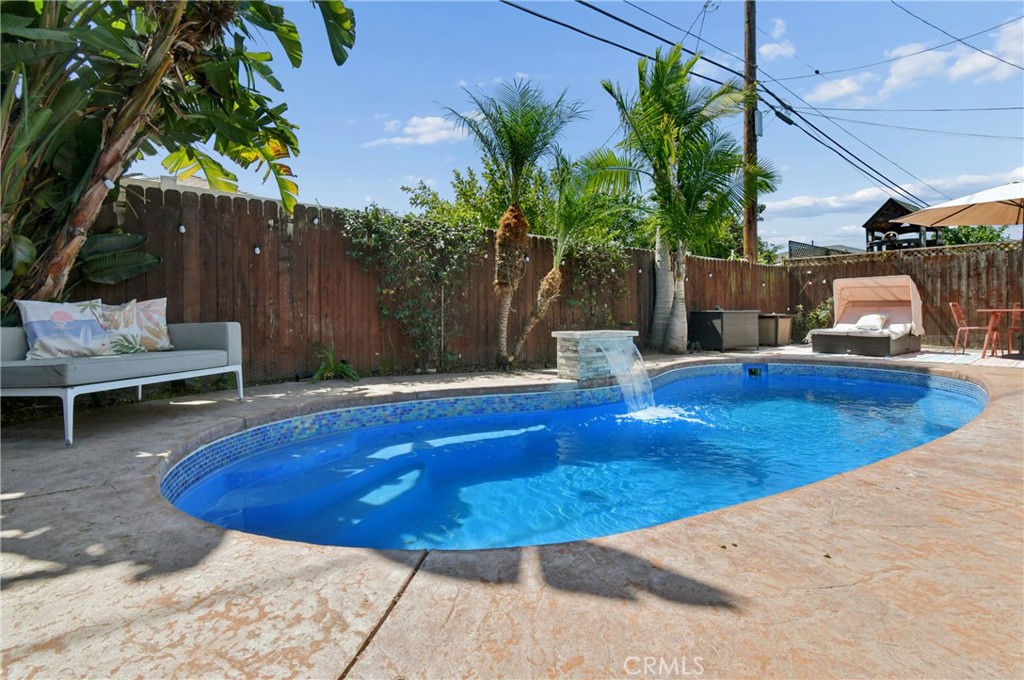 Backyard swimming pool with a stone waterfall, patio seating, and tropical palms.