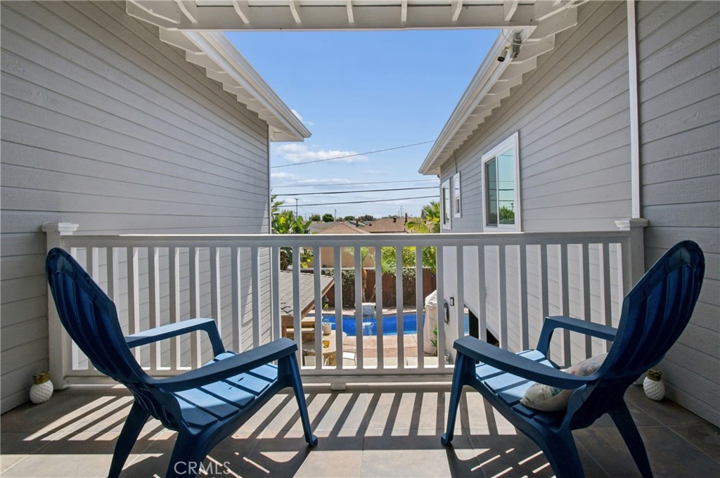Covered balcony with two blue chairs overlooking a backyard pool.
