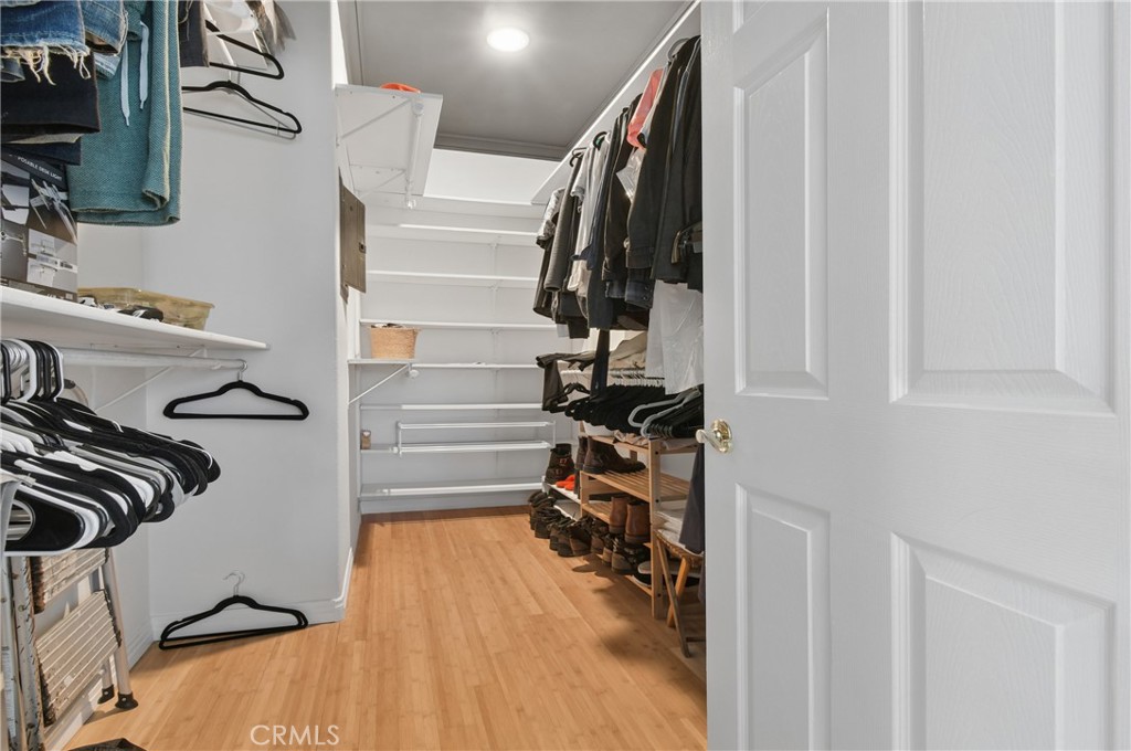 Walk-in closet with built-in shelving, hanging clothes, and shoes along the aisle.