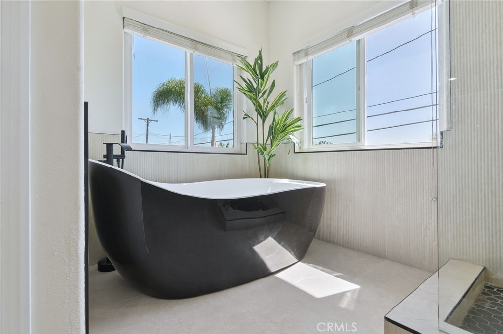 Bathroom with a black freestanding tub beneath corner windows and a glass-enclosed shower.