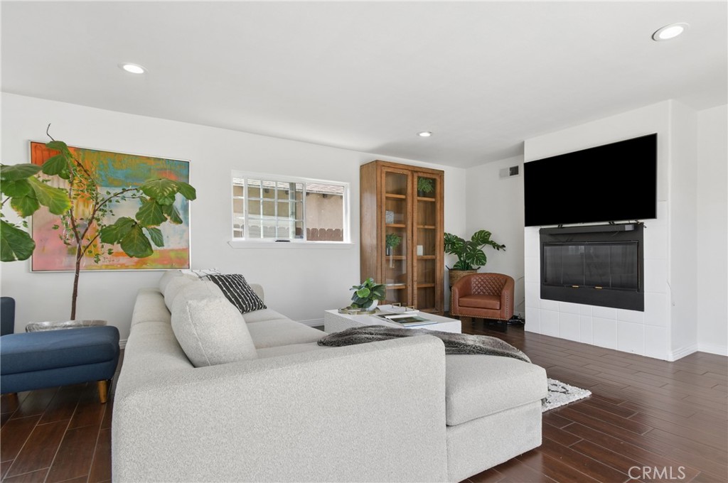 Staged living room with a white sectional, colorful artwork, and a television above the fireplace.