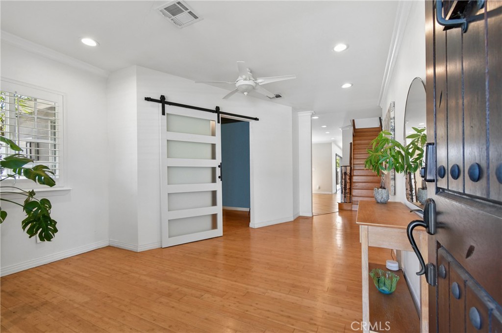 Bright entryway with hardwood floors, a frosted-glass barn door, and a staircase.