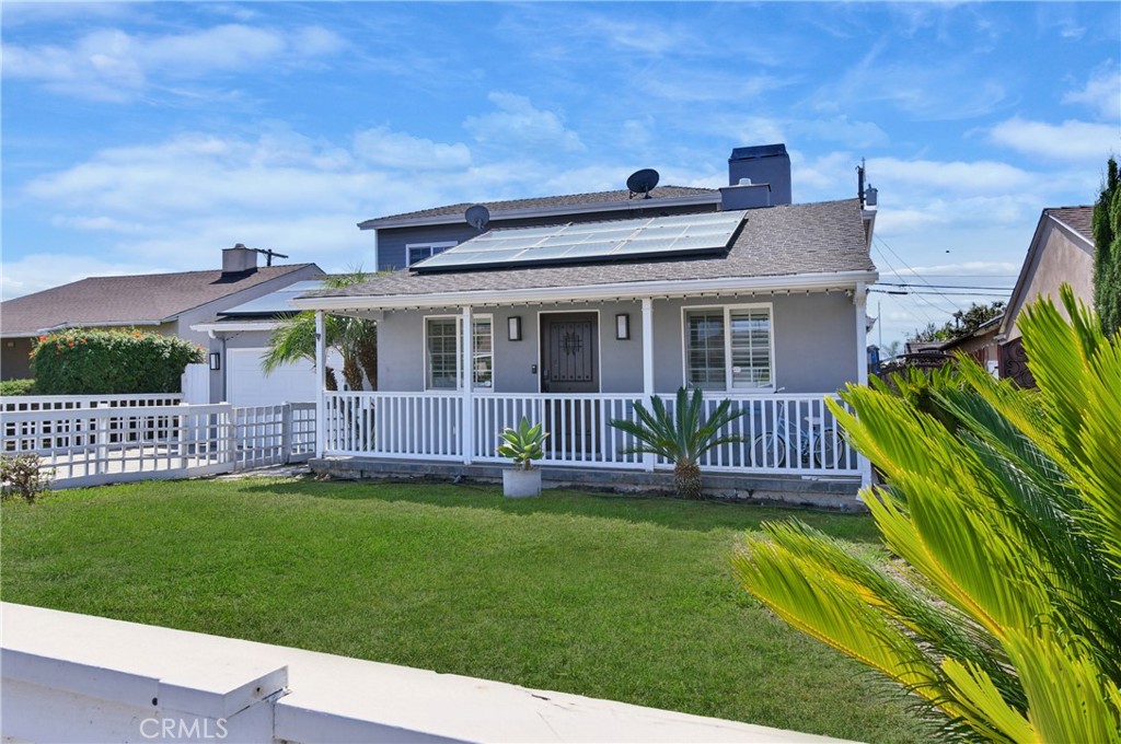 Gray house with rooftop solar panels, a white-railed porch, and a green front lawn.
