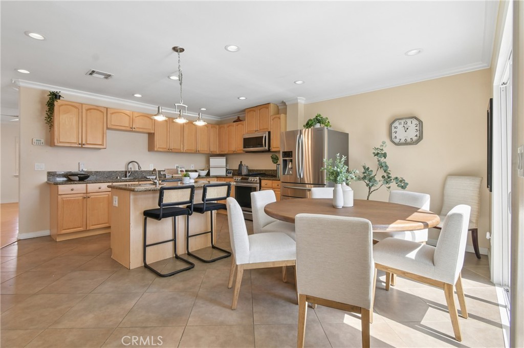 Open-plan kitchen and dining area with light wood cabinets, stainless appliances, and a round table.