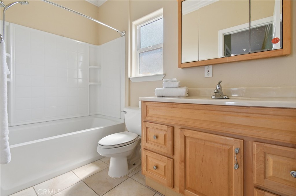 Bathroom with a white tub and shower, toilet, and wood vanity beneath a large mirror.