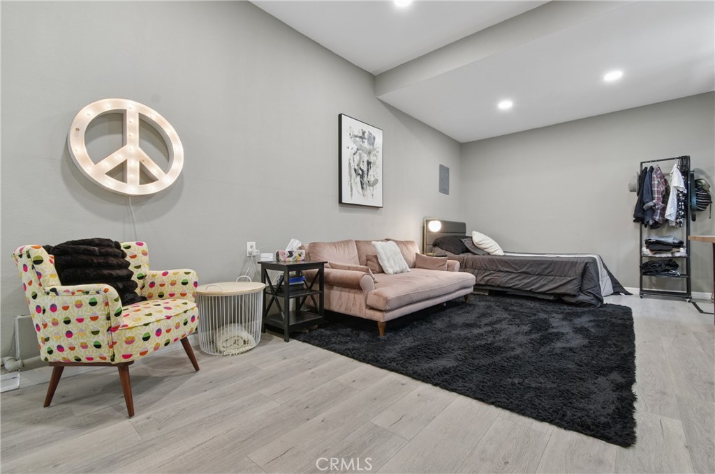 Furnished bedroom with a blush sofa, colorful armchair, and illuminated peace sign above a black rug.