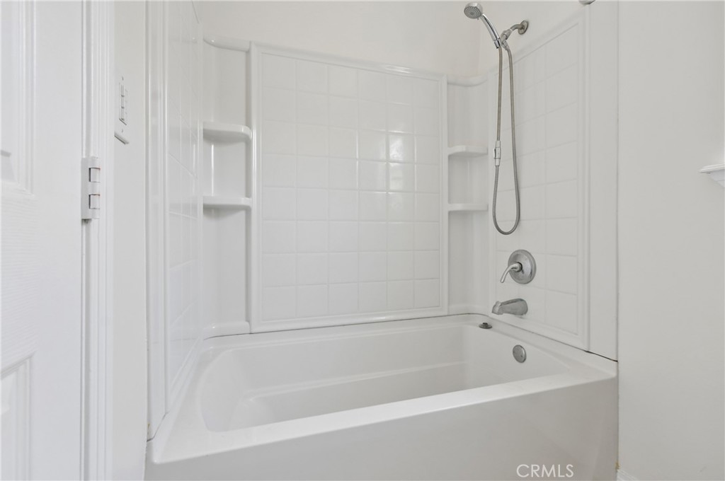 White bathtub and shower with tiled walls and built-in corner shelves.