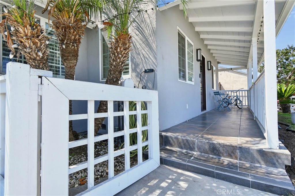 Gray house porch with white railings, tiled steps, and a covered walkway lined with palm trees.
