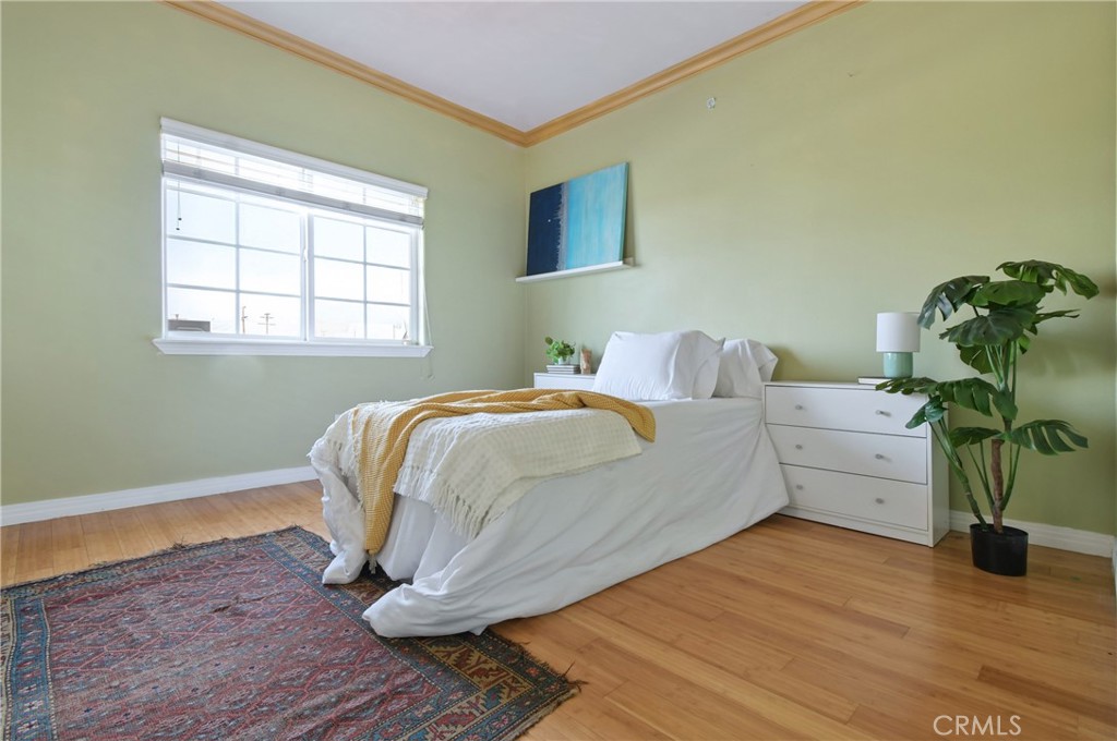 Staged bedroom with a white bed, pale green walls, hardwood floors, and a patterned rug.